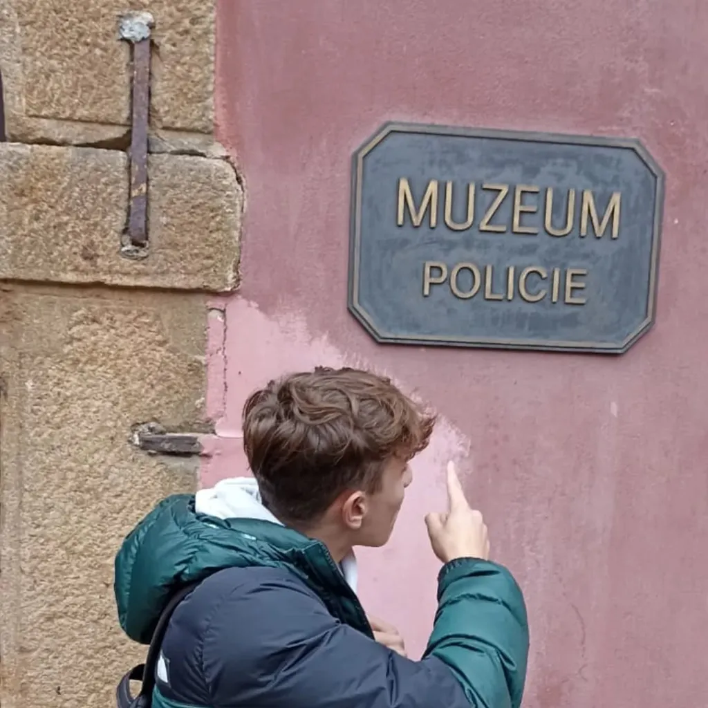 Žák ukazuje na ceduli Muzeum Policie na fasádě budovy.
