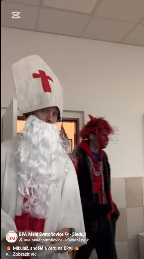 Žák převlečený za Mikuláše a žák v kostýmu čerta na chodbě školy.