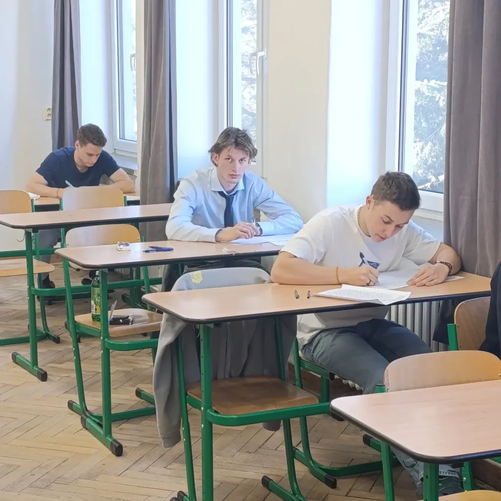 Žáci píší písemnou maturitní zkoušku v lavicích učebny.